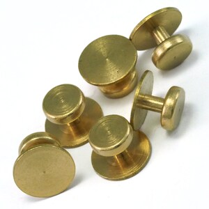 May include: Six gold-toned metal button fasteners with a round head and a post. The fasteners are arranged in a cluster on a white surface.