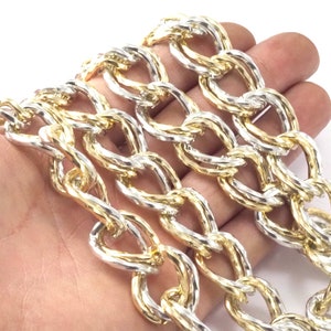Può includere: Primo piano di una collana a catena dorata e argentata. La catena è composta da maglie ovali intrecciate con un design a torsione.
