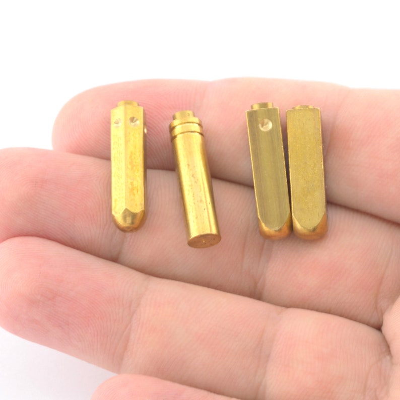 May include: Four gold-colored metal rods with rounded ends. The rods are arranged in a row on a hand.