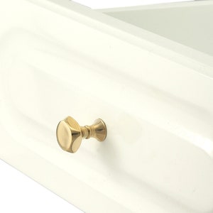 Può includere: Un cassetto bianco con una manopola dorata. La manopola è di design semplice e rotondo, con un bordo leggermente rialzato.