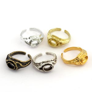 Puede incluir: Cinco anillos ajustables en tonos plata, oro y bronce. Cada anillo presenta un engaste abierto, perfecto para la creación de joyas. Los anillos tienen superficies texturizadas y diseños variados.