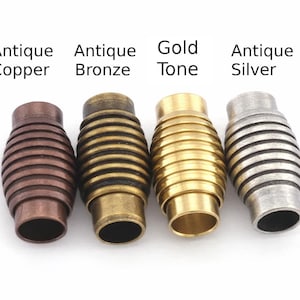 May include: Four metal magnetic clasps in antique copper, antique bronze, gold tone, and antique silver. Each clasp is barrel-shaped with horizontal ridges. Text above each clasp indicates the color.