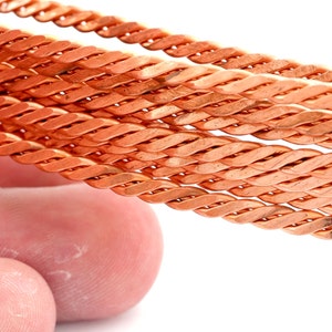 May include: Close-up of a braided copper wire. The wire is twisted together to create a rope-like texture.