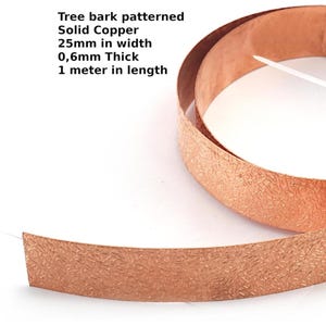 May include: A roll of solid copper with a tree bark pattern. The copper strip is 2.5cm wide, 0.6mm thick, and 1 meter in length. The copper has a textured surface and a warm, reddish-brown colour.
