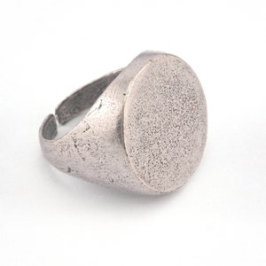 May include: A silver ring with a large, round, flat top. The ring has a textured finish.