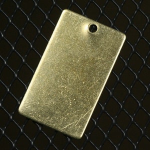 May include: A gold-colored metal tag with a hole punched in the top. The tag has a slightly textured surface.