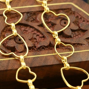 May include: Two gold heart-shaped chains on a wooden surface. The chains are made of interlocking hearts.