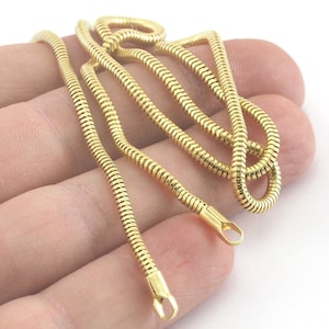 Könnte beinhalten: Eine goldene Schlangenkettenkette mit glänzendem Finish. Die Kette besteht aus ineinandergreifenden Gliedern, die einen glatten, fließenden Look erzeugen.
