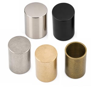 May include: A set of five cylindrical knobs in various finishes, including polished silver, matte black, brushed nickel, brushed gold, and an antique brass finish. Each knob features a flat top and a smooth, solid, vertical side profile.