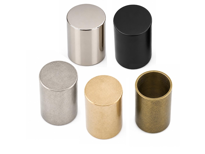 May include: A set of five cylindrical knobs in various finishes, including polished silver, matte black, brushed nickel, brushed gold, and an antique brass finish. Each knob features a flat top and a smooth, solid, vertical side profile.