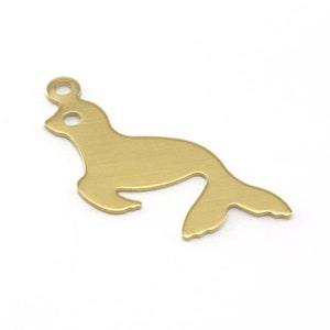 May include: Gold metal charm shaped like a seal. The charm has a hole at the top for attaching to a necklace or bracelet.