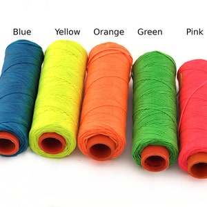 Puede incluir: Cinco carretes de hilo de diferentes colores: azul, amarillo, naranja, verde y rosa. Los carretes son todos del mismo tamaño y forma, y están dispuestos en una fila de izquierda a derecha.