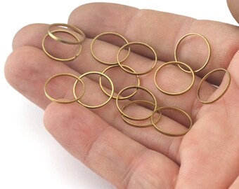May include: A collection of 15 gold-colored metal jump rings, approximately 1/2 inch in diameter, are scattered on a hand.