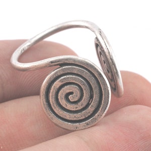 Puede incluir: Anillo de plata con un diseño en espiral. El anillo está hecho de una sola pieza de metal que se retuerce en forma de espiral.