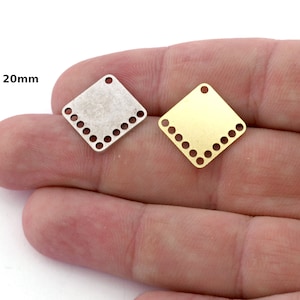 May include: Two 20mm square metal charms with a decorative border of holes. One charm is silver and the other is gold.