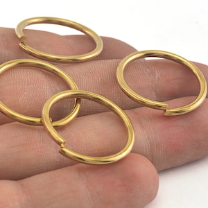 May include: Four gold-colored metal key rings, each with a split ring design, are displayed on a hand.