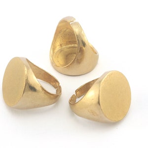 May include: Three gold-colored adjustable signet rings with a matte finish. Each ring features a round, flat face and a simple band. The rings are displayed on a white background, showcasing their design.