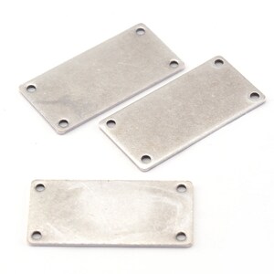May include: Three silver metal rectangular plates with rounded corners and four holes each. The plates are on a white background.