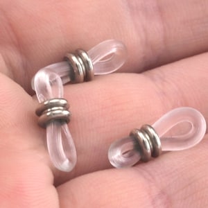May include: Three clear plastic eyeglass strap holders with silver metal rings. The holders are designed to keep glasses from slipping off the ears.