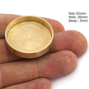 Könnte beinhalten: Ein kleines, rundes Metallteil in Messingfarbe mit einer vertieften Mitte. Das Teil hat einen Durchmesser von 32 mm, ein Loch von 30 mm und eine Tiefe von 5 mm. Das Teil wird in einer Hand gehalten.