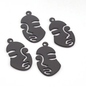 May include: Four black metal face charms with a simple line art design. The charms are oval shaped and have a hole at the top for hanging.