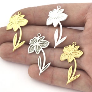 May include: Four metal flower charms in gold and silver. The charms are shaped like daffodils with a detailed design. They are perfect for jewelry making or crafting.