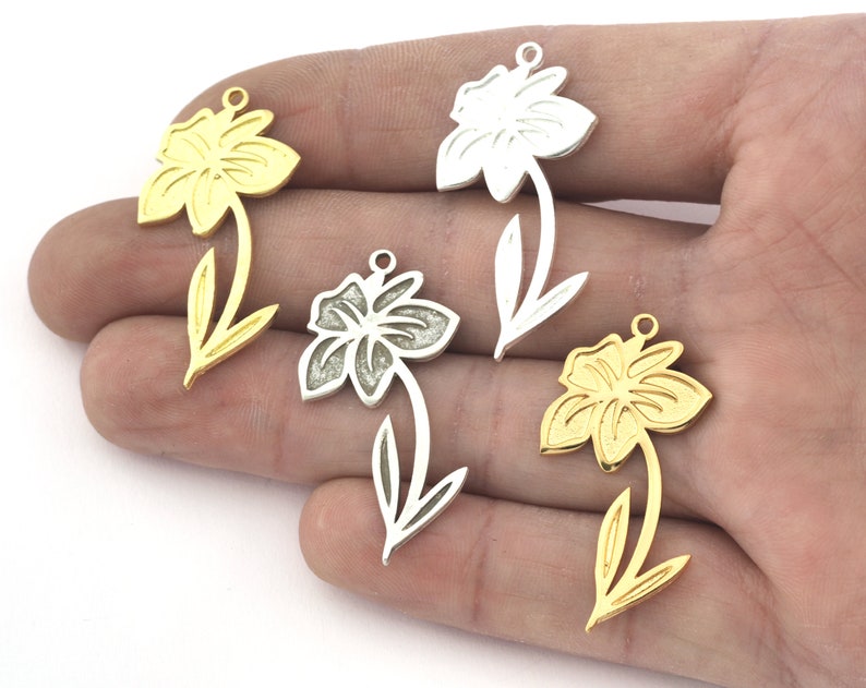May include: Four metal flower charms in gold and silver. The charms are shaped like daffodils with a detailed design. They are perfect for jewelry making or crafting.