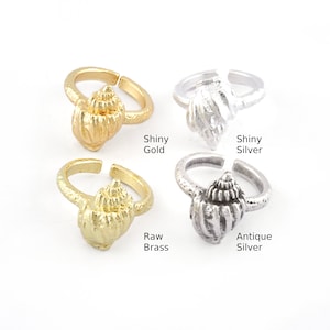 May include: Four adjustable rings featuring a seashell design in four different finishes: shiny gold, shiny silver, raw brass, and antique silver.