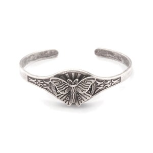 May include: A silver cuff bracelet with a detailed butterfly design at the centre. The butterfly is set against a sunburst pattern, with decorative etched details along the band. The bracelet has an open design for easy wear.