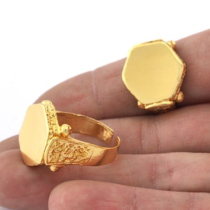 Könnte beinhalten: Zwei goldene Ringe mit sechseckigem Design. Die Ringe sind schlicht und haben eine glatte Oberfläche. Die Ringe befinden sich auf einer Hand.