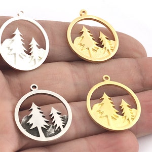 Può includere: Quattro ciondoli rotondi con un design a forma di foresta ritagliata. Due sono argentati e due dorati. Ogni ciondolo presenta una catena montuosa e due pini all'interno di una cornice circolare, con un piccolo anello in alto per appenderlo.
