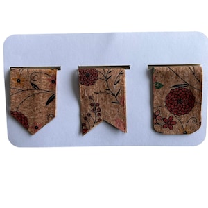 May include: Three cork bookmarks with floral patterns in shades of brown and red. The bookmarks are shaped like flags with pointed ends.
