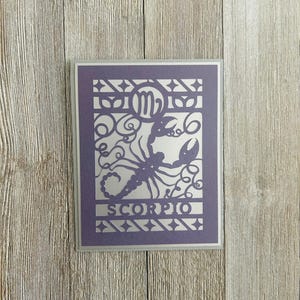 Może przedstawiać: Fioletowa karta z wyciętym wzorem znaku zodiaku Skorpion, w tym symbolem konstelacji i skorpionem. Na karcie widnieje napis "SCORPIO" u dołu.