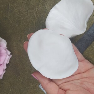 Puede incluir: Dos piezas blancas, redondas y en forma de pétalo de arcilla polimérica, utilizadas para la elaboración de flores artificiales.