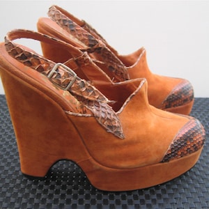 Könnte beinhalten: Ein Paar orangefarbene Wildleder-Wedgesandalen mit Schlangenmuster-Akzenten. Die Sandalen haben einen Slingback-Riemen mit einer silbernen Schnalle und eine Plateausohle. Zehen und Ferse haben ein Schlangenmuster.