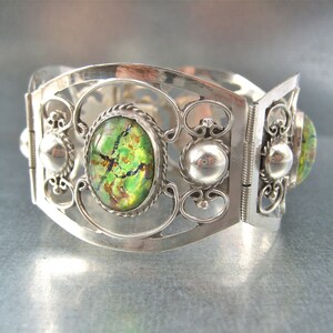 Könnte beinhalten: Ein silbernes Armband mit filigranem Design und drei grünen, irisierenden ovalen Steinen.