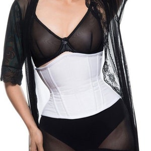 Puede incluir: Un corsé blanco con una superposición de encaje negro y una liga negra. La modelo lleva medias rosas con un tatuaje en la pierna.