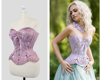 May include: A lavender corset with delicate floral embroidery and gold chain accents. The corset is strapless and has a sweetheart neckline. It is shown on a mannequin and a person wearing it.