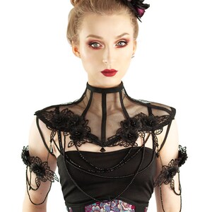 Puede incluir: Un collar de encaje negro con adornos florales y un par de pu&ntilde;os a juego. El collar tiene un dise&ntilde;o de malla y est&aacute; adornado con cuentas negras. La modelo lleva una blusa negra y un cors&eacute; con estampado floral.