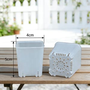 May include: Two small, translucent plastic plant pots, each measuring 4 cm wide and 5 cm tall. One pot is upright, the other is on its side, showing drainage holes. The pots are on a wooden surface, with a white picket fence in the background.