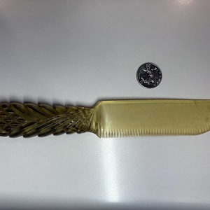 May include: A vintage butter knife with a decorative handle and a serrated blade. The handle has a carved, textured design. The knife is a light amber color. A quarter is next to the knife for size comparison.