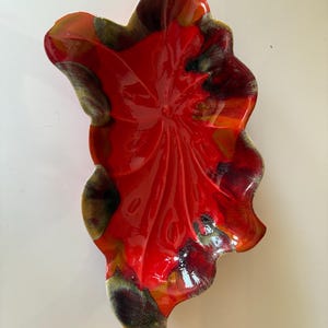 May include: A glossy, leaf-shaped ceramic dish with a vibrant red interior and a multi-toned exterior. The dish features a detailed, textured surface and a flowing, organic design. The rim showcases shades of green, brown, and orange.
