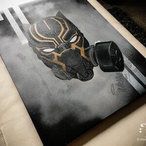 Puede incluir: Obra de arte en aerosol negro y dorado de una m&aacute;scara de Black Panther con una m&aacute;scara de gas. La obra de arte est&aacute; en un lienzo y tiene un fondo blanco con l&iacute;neas negras.