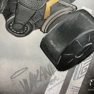 Puede incluir: Primer plano de una m&aacute;scara de gas negra con un acento dorado. La m&aacute;scara tiene un filtro redondo unido al lado. El fondo es un lienzo gris claro con un patr&oacute;n blanco y gris.