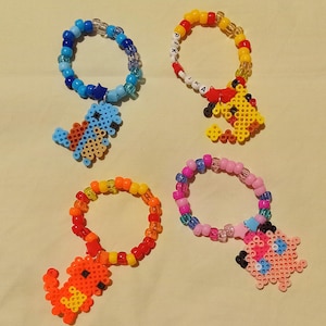May include: Four colorful beaded bracelets with pixelated cartoon characters attached. The bracelets are made of small plastic beads in various colors, including blue, yellow, red, orange, and pink. The characters are Pikachu, Squirtle, Charmander, and Bulbasaur.