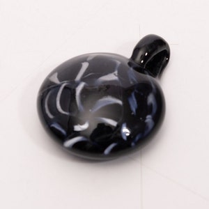 May include: A black glass pendant with white and blue swirls. The pendant has a loop at the top for attaching to a chain.
