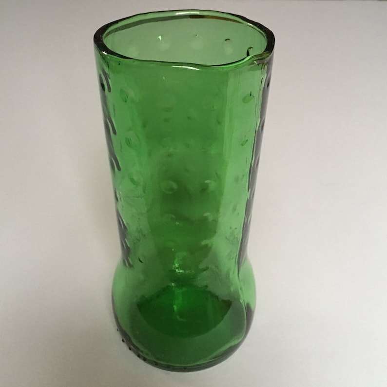 May include: A green glass vase with a textured surface. The vase has a wide mouth and a rounded bottom.