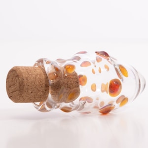 May include: A clear glass bottle with a cork stopper. The bottle is decorated with small, orange and brown bubbles.