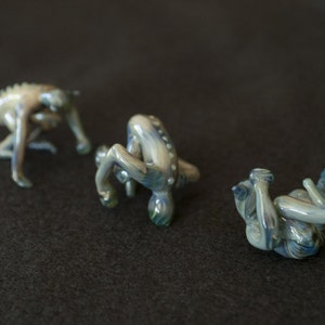 Puede incluir: Tres pequeñas figuritas de vidrio en varias poses, cada una con un acabado marmoleado azul y verde.