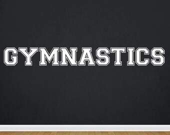 May include: White text on a black background reads "GYMNASTICS" in a collegiate font style. The background is a wall with a white baseboard and a wood floor.